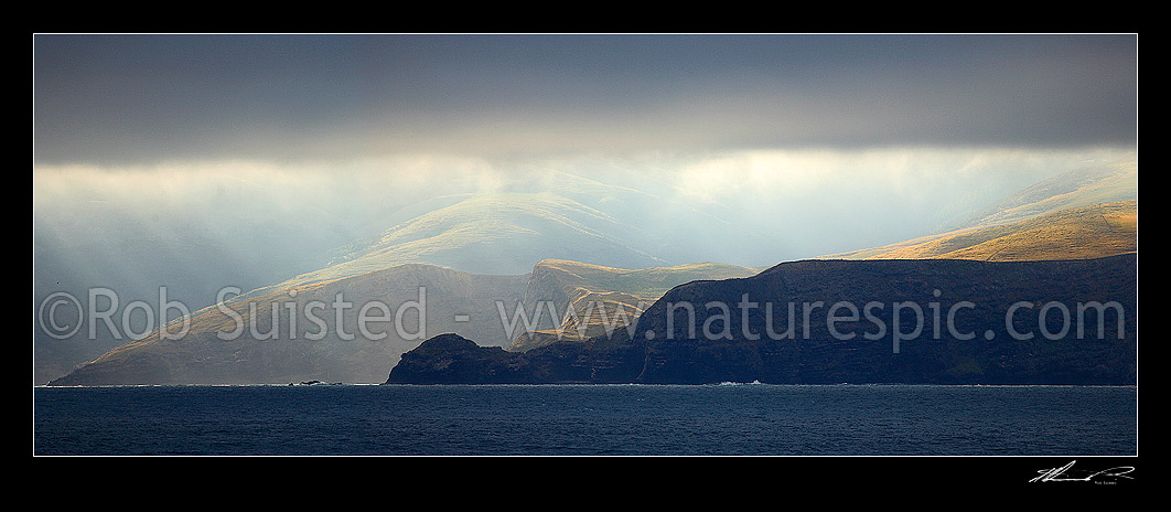 Image of Banks Peninsula coastline with dramatic sun shining under coastal cloud. Panorama, Banks Peninsula, Christchurch City District, Canterbury Region, New Zealand (NZ) stock photo image