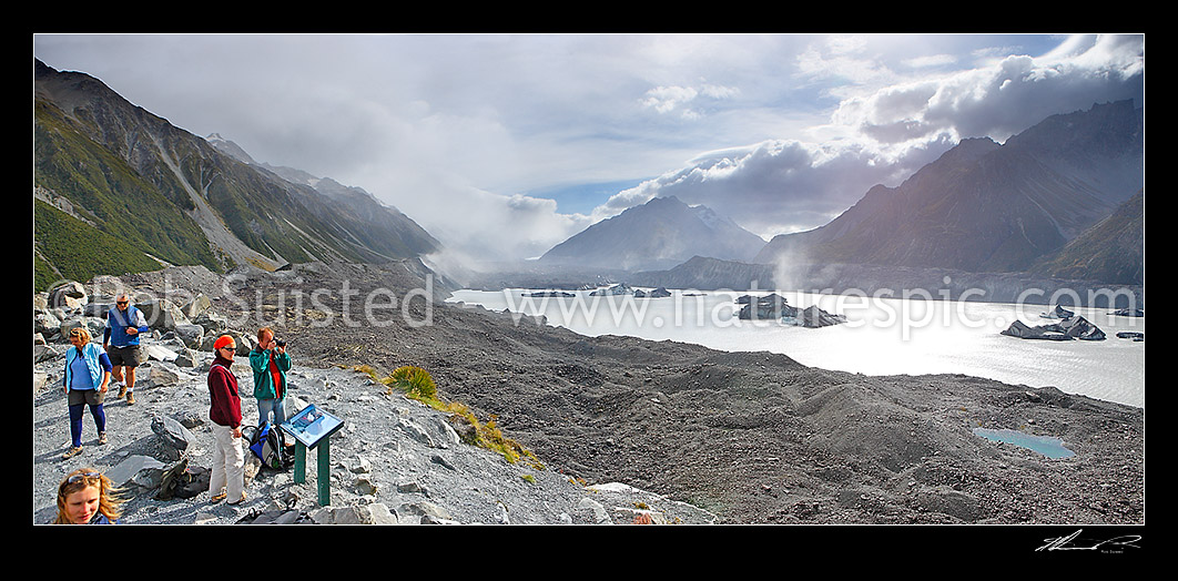 Image of Tourist visitors at lookout above the Tasman Glacier moraine and terminal lake. Aoraki Mount Cook Range left, Burnett Range right. Tasman Valley. Dust wind storms, Aoraki / Mount Cook National Park, MacKenzie District, Canterbury Region, New Zealand (NZ) stock photo image