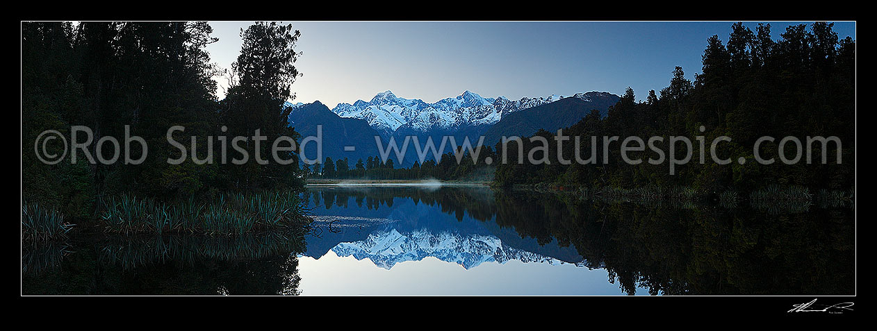 Image of Lake Matheson. Pre-dawn morning calm reflections on lake with Aoraki / Mount Cook (right;3754m) and Mount Tasman (left;3498m). Morning mist. Panorama, Westland National Park, Westland District, West Coast Region, New Zealand (NZ) stock photo image