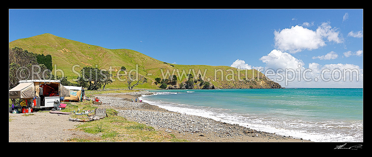 Image of Port Jackson beach and campsite with Kaiiti Point beyond. Family with children playing in surf in summertime. Tents and caravans on foreshore. Panorama, Cape Colville, Thames-Coromandel District, Waikato Region, New Zealand (NZ) stock photo image