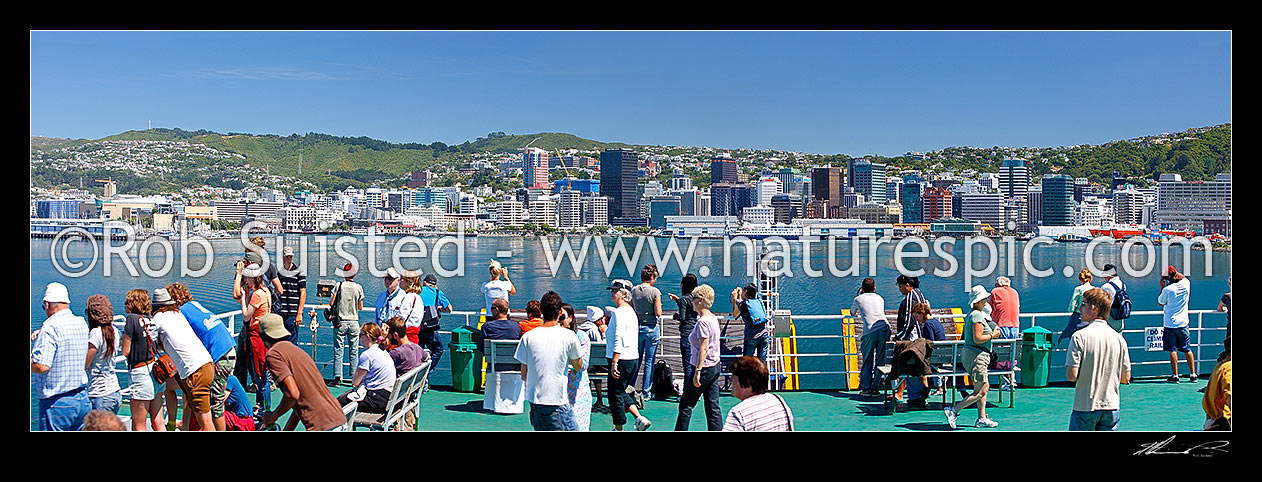 Image of Wellington City skyline panorama from a Cook Strait ferry departing the capital city. Travellers photographing view from deck in summer sun, Wellington City, Wellington City District, Wellington Region, New Zealand (NZ) stock photo image