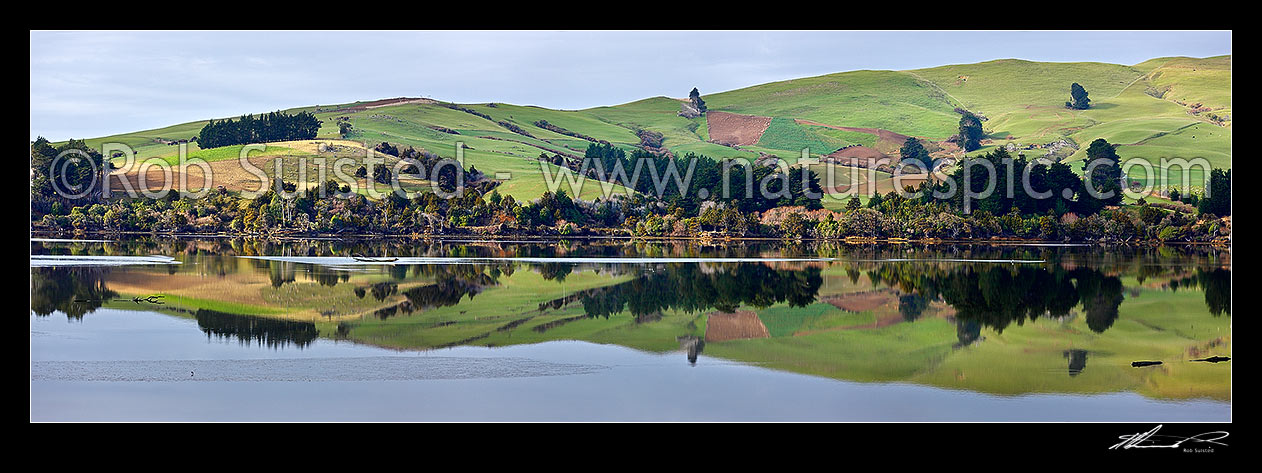 Image of Farmland and rolling pasture reflected in the Catlins Lake. Hinahina Hill. Panorama, Owaka, Clutha District, Otago Region, New Zealand (NZ) stock photo image