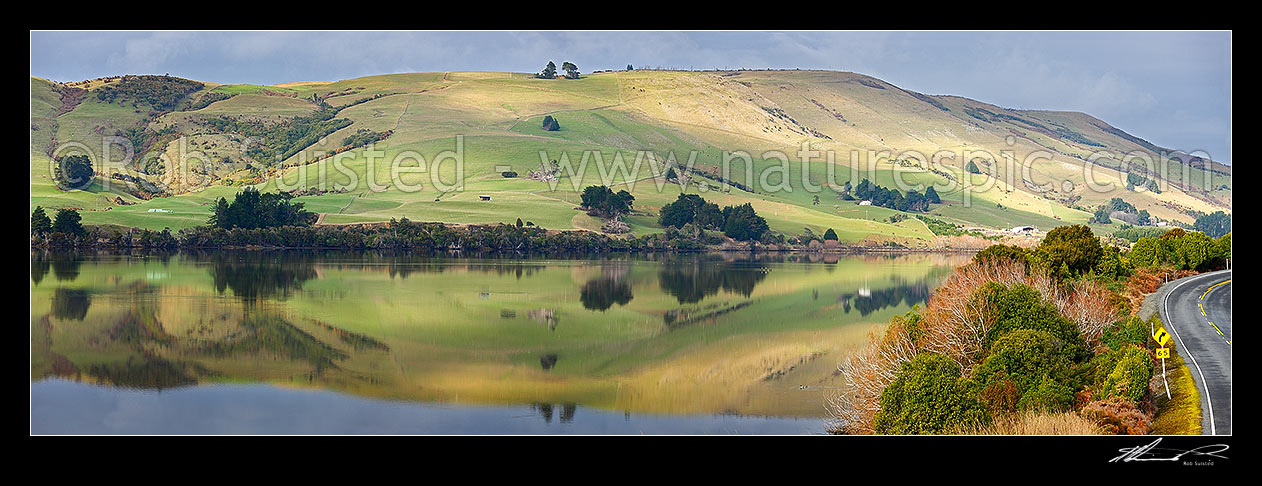 Image of Farmland and rolling pasture reflected in the Catlins Lake. Hinahina Hill. Panorama, Owaka, Clutha District, Otago Region, New Zealand (NZ) stock photo image