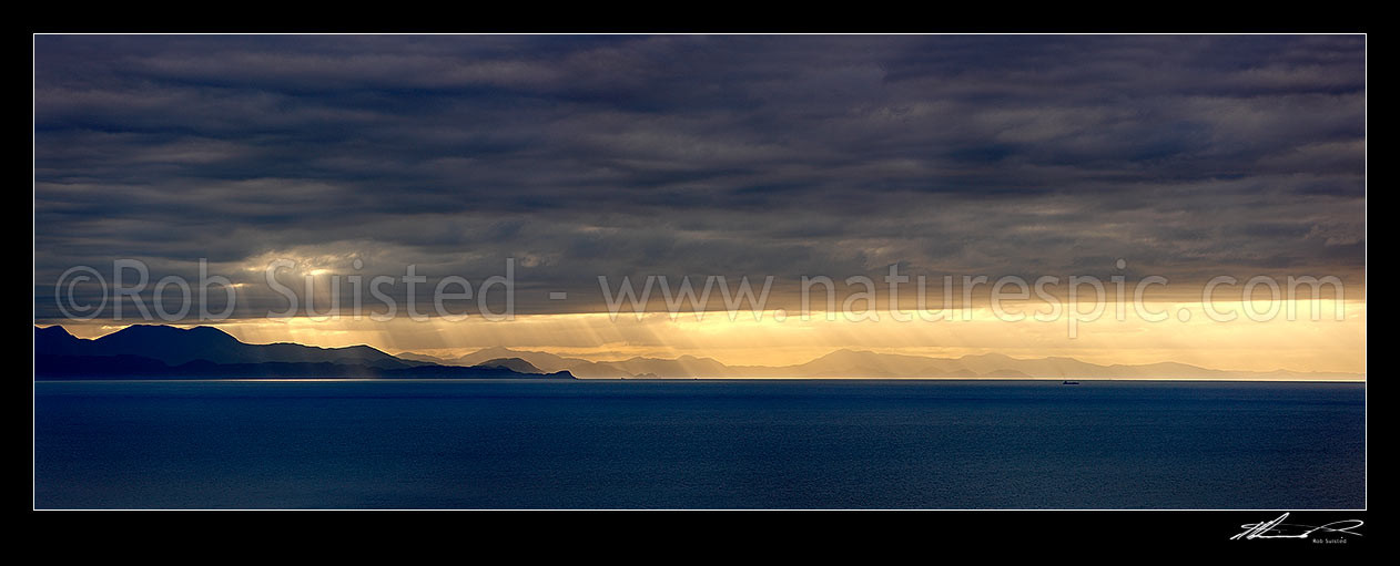 Image of Looking across Cook Strait from Mana Island to the South Island with dramatic sun poking through clouds over entrances to the Marlborough Sounds. Panorama, Mana Island, Porirua City District, Wellington Region, New Zealand (NZ) stock photo image