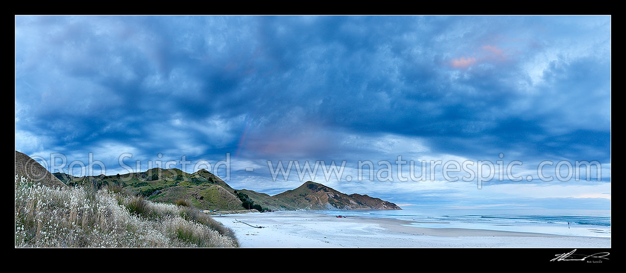 Image of Kaiaua Bay Beach moody sunset panorama as rain starts and storm clouds gather, with Marau Point centre. People retrieving or launching small boat, Tolaga Bay, Gisborne District, Gisborne Region, New Zealand (NZ) stock photo image