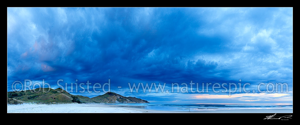 Image of Kaiaua Bay Beach moody twilight panorama as rain starts and storm clouds gather, with Marau Point centre. Surf casting fishing rod on beach, Tolaga Bay, Gisborne District, Gisborne Region, New Zealand (NZ) stock photo image