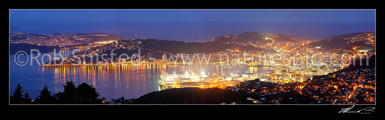 Image of Wellington City at night. Central business district (CBD), buildings, harbour and suburbs glowing with lights after dark. Panorama, Wellington, Wellington City District, Wellington Region, New Zealand (NZ) stock photo image