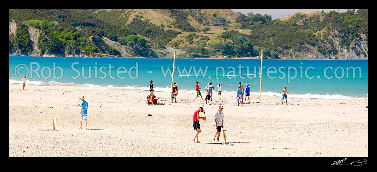 Image of Beach volleyball game and beach cricket match on Anaura Bay beach during summer holidays. Young kids and families enjoying the beach. Panorama, Anaura Bay, East Coast, Gisborne District, Gisborne Region, New Zealand (NZ) stock photo image