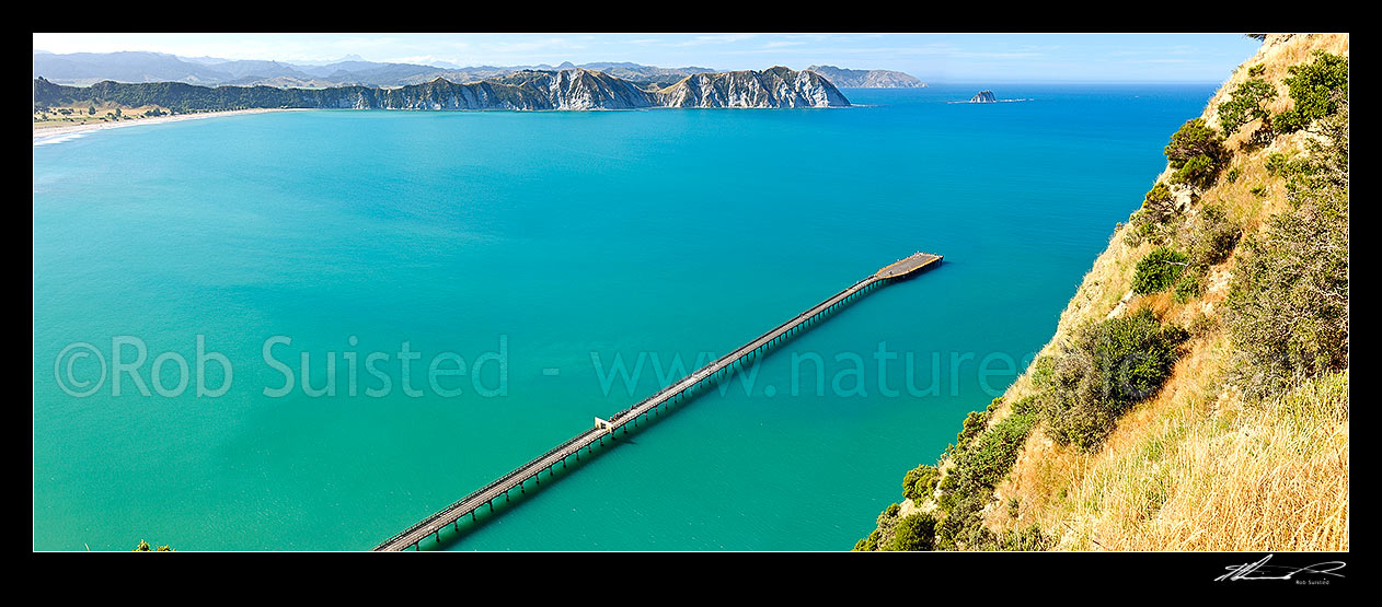 Image of Tolaga Bay wharf stretching into Tolaga Bay. New Zealand's longest wharf at 660 metres in length. Te Karaka Point beyond, with Marau Point distant. Panorama, Tolaga Bay, East Coast, Gisborne District, Gisborne Region, New Zealand (NZ) stock photo image