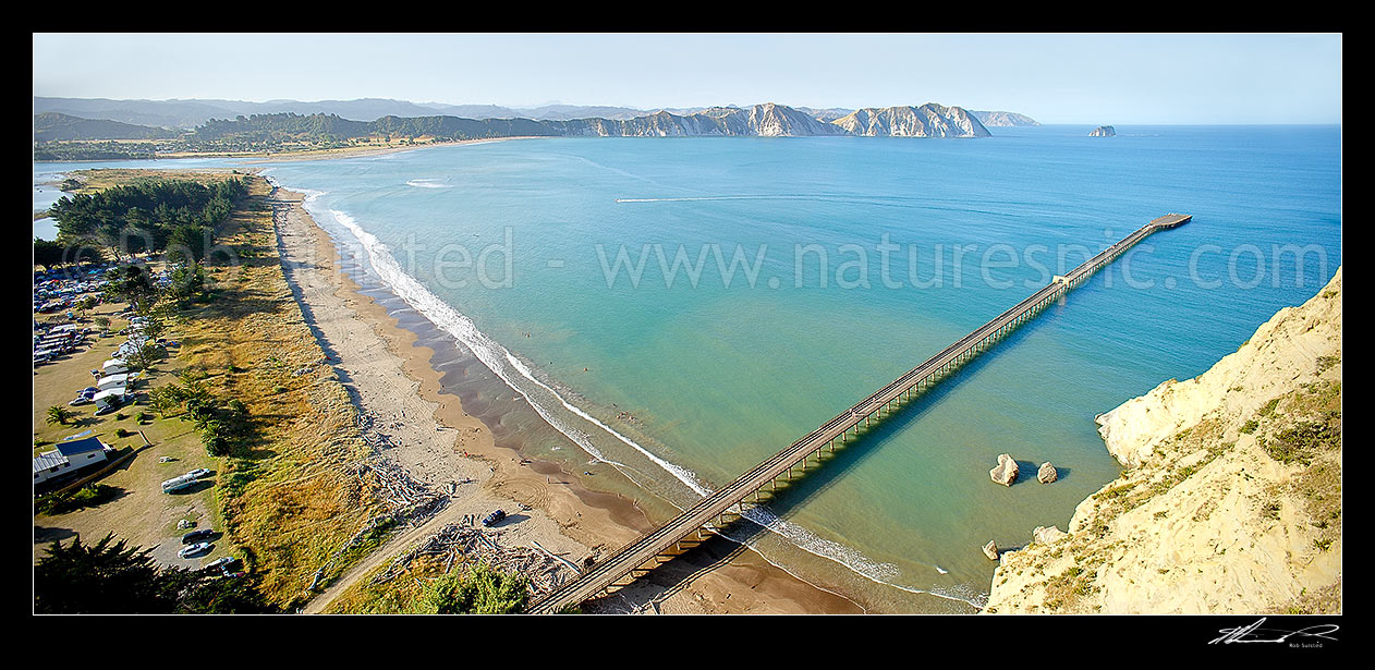 Image of Tolaga Bay wharf in Tolaga Bay. Uawa River mouth and town top left. NZ's longest wharf at 660 metres. Mt Hikurangi distant centre. Panorama, Tolaga Bay, East Coast, Gisborne District, Gisborne Region, New Zealand (NZ) stock photo image