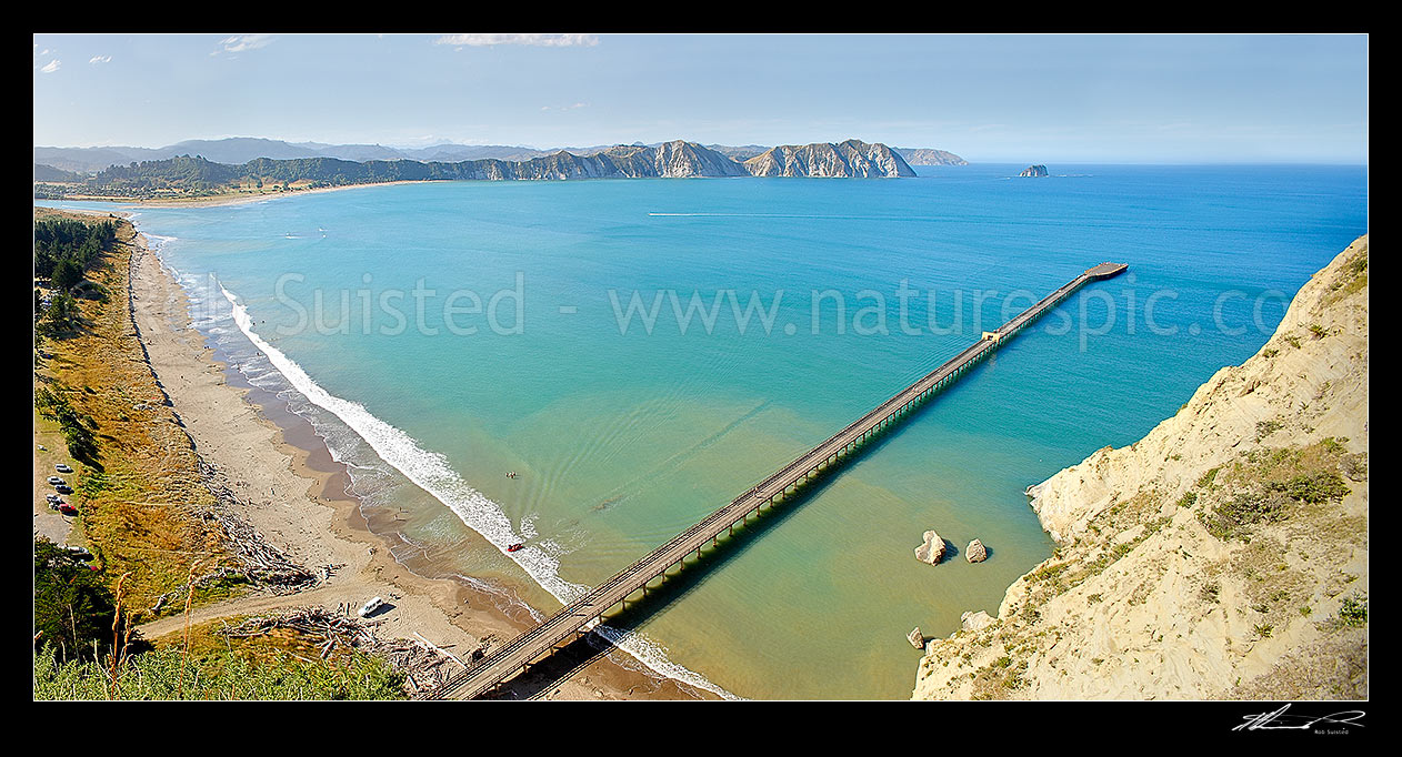 Image of Tolaga Bay wharf in Tolaga Bay. Uawa River mouth and town top left. NZ's longest wharf at 660 metres. Mt Hikurangi distant centre left. Panorama, Tolaga Bay, East Coast, Gisborne District, Gisborne Region, New Zealand (NZ) stock photo image