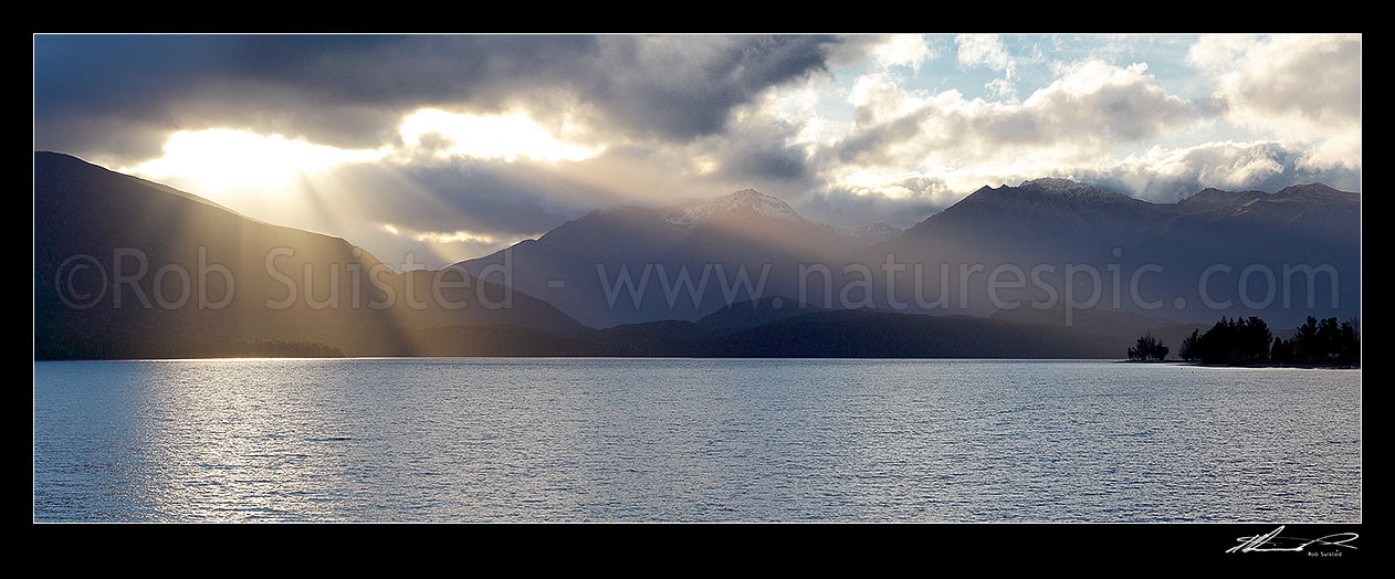 Image of Lake Te Anau and Fiordland with sun rays breaking through cloud near Brod Bay. Murchison Mountains centre and Bluegum Point right. Panorama, Fiordland National Park, Southland District, Southland Region, New Zealand (NZ) stock photo image