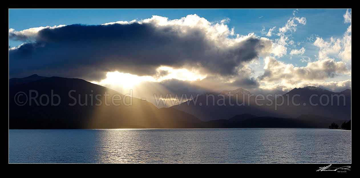 Image of Lake Te Anau and Fiordland with sun rays breaking through cloud near Brod Bay. Murchison Mountains centre and Bluegum Point right. Panorama, Fiordland National Park, Southland District, Southland Region, New Zealand (NZ) stock photo image