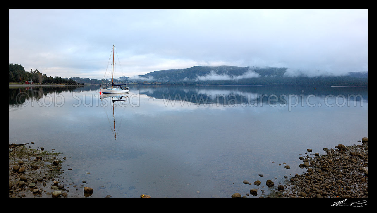 Image of Sailboat moored on Lake Te Anau on a calm winter morning, with perfect reflection. Fiordland National Park beyond. Panorama, Te Anau, Southland District, Southland Region, New Zealand (NZ) stock photo image