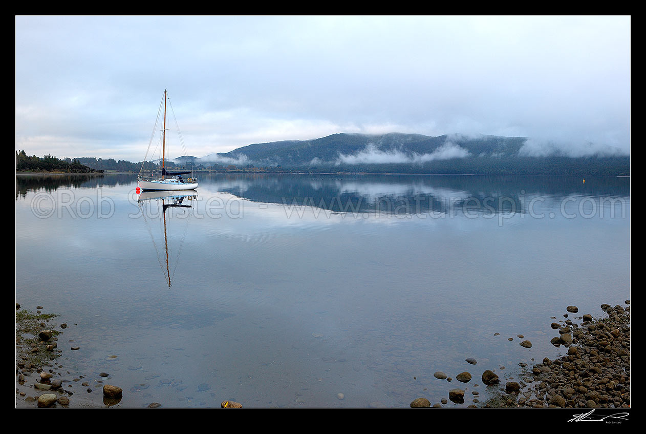 Image of Sailboat moored on Lake Te Anau on a calm winter morning, with perfect reflection. Fiordland National Park beyond. Panorama, Te Anau, Southland District, Southland Region, New Zealand (NZ) stock photo image