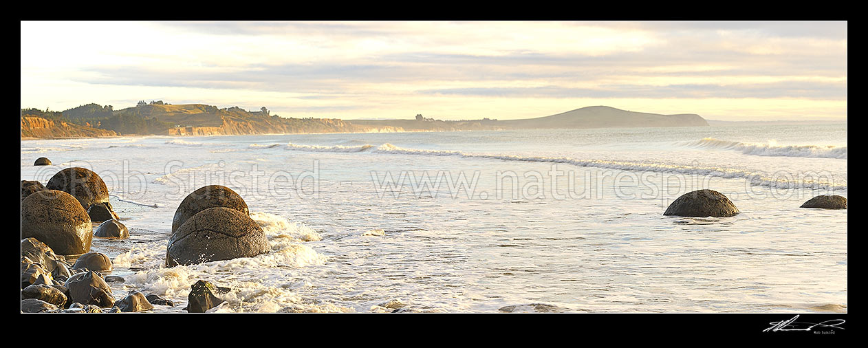 Image of Moeraki Boulders / Kaihinaki, 60 Million year old mudstone concretions at sunrise with Lookout Bluff distant right. Panorama, Moeraki, Waitaki District, Canterbury Region, New Zealand (NZ) stock photo image