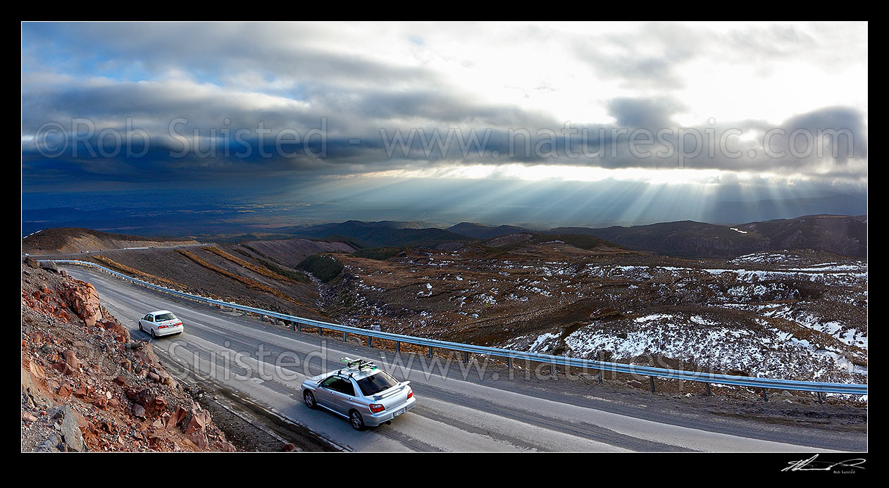 Image of Ohakune Mountain Road with stunning sun shafts illuminating flanks of Mount Ruapehu and Ohakune far below. Turoa Skifield road. Panorama, Tongariro National Park, Ruapehu District, Manawatu-Wanganui Region, New Zealand (NZ) stock photo image