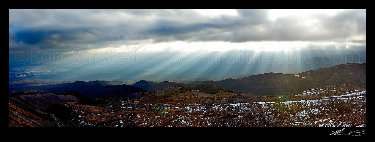 Image of Ohakune (far left), farmland and flanks of Mount Ruapehu being lit by sun shafts behind a passing weather front. Maungaturuturu, Makotuku Rivers and Lake Surprise far right. Panorama, Tongariro National Park, Ruapehu District, Manawatu-Wanganui Region, New Zealand (NZ) stock photo image