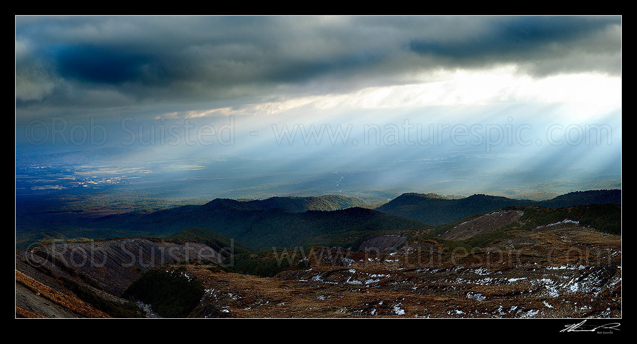 Image of Ohakune (far left), farmland and flanks of Mount Ruapehu being lit by sun shafts behind a passing weather front. Maungaturuturu River valley. Panorama, Tongariro National Park, Ruapehu District, Manawatu-Wanganui Region, New Zealand (NZ) stock photo image