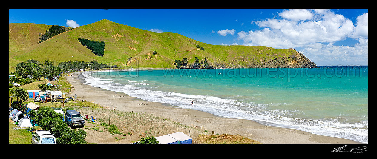 Image of Port Jackson bay beach and Departmenf of Conservation (DOC) campsite with summer campers and tents on foreshore. Kaiiti Point behind. Panorama, Cape Colville, Thames-Coromandel District, Waikato Region, New Zealand (NZ) stock photo image