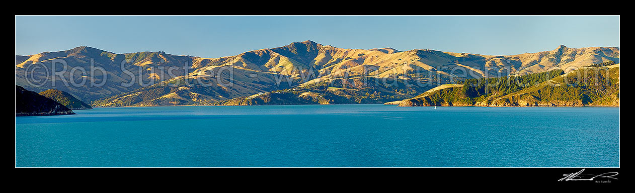 Image of Akaroa upper harbour with Mt Pearce and Duvauchelle at left, Duvauchelle Peak (738m) and Robinsons Bay centre, and Takamatua with passing sailboat (right) from near Wainui. Banks Peninsula. Panorama, Akaroa, Christchurch City District, Canterbury Region, New Zealand (NZ) stock photo image