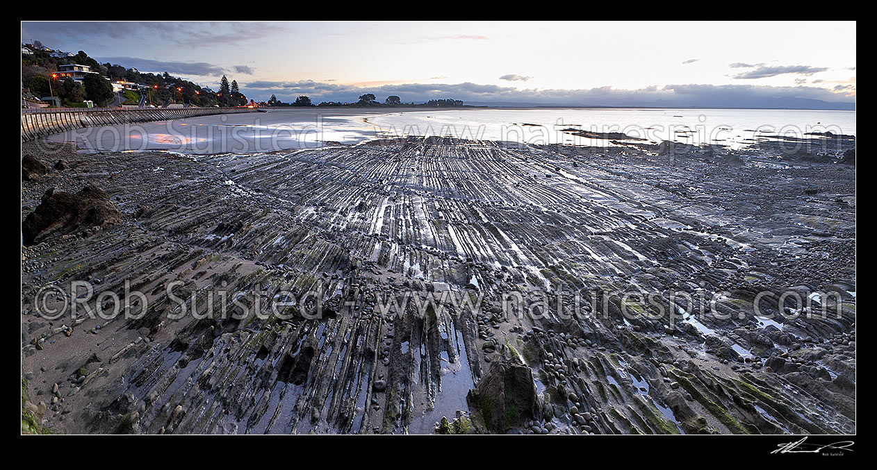 Image of Tahunanui Beach evening sunset panorama with dramatic geologial rock patterns in foreground, Nelson, Nelson City District, Nelson Region, New Zealand (NZ) stock photo image