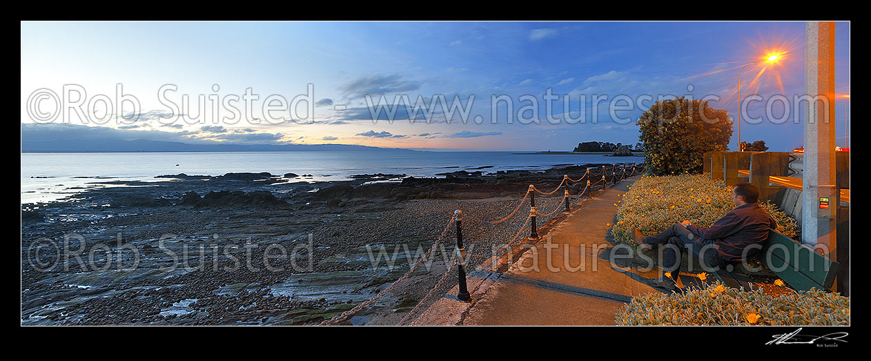 Image of Tahunanui Beach waterfront walkway along Rocks Road and Wakefield Quay, with person watching sunset over Tasman Bay. Panorama, Nelson, Nelson City District, Nelson Region, New Zealand (NZ) stock photo image