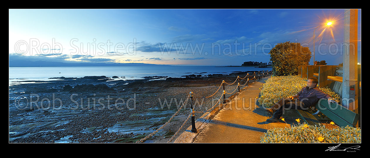 Image of Tahunanui Beach waterfront walkway along Rocks Road and Wakefield Quay, with person watching sunset over Tasman Bay. Panorama, Nelson, Nelson City District, Nelson Region, New Zealand (NZ) stock photo image