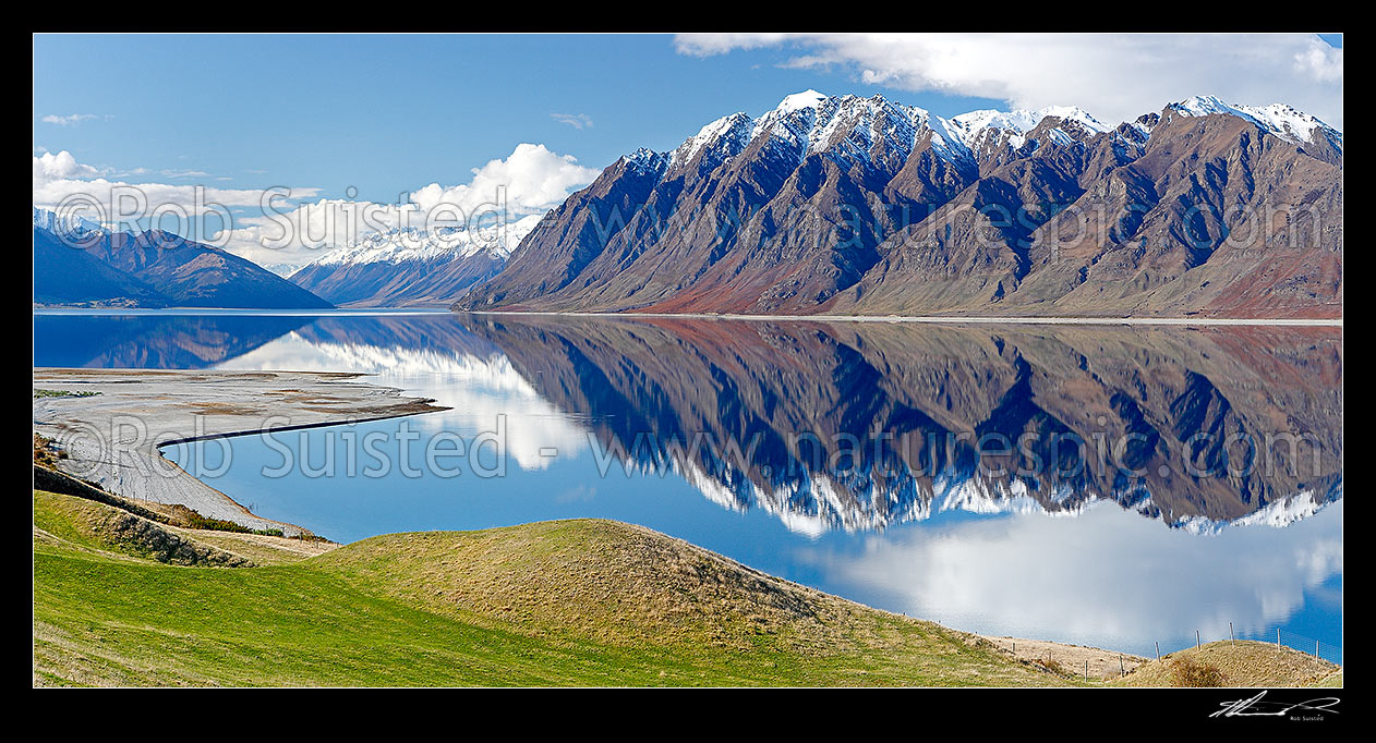 Image of Lake Hawea and farmland with mountains reflecting the surrounding snowy ranges, looking towards Huxley Range, Dingle Burn and Hunter valley. Panorama, Lake Hawea, Otago, Queenstown Lakes District, Otago Region, New Zealand (NZ) stock photo image