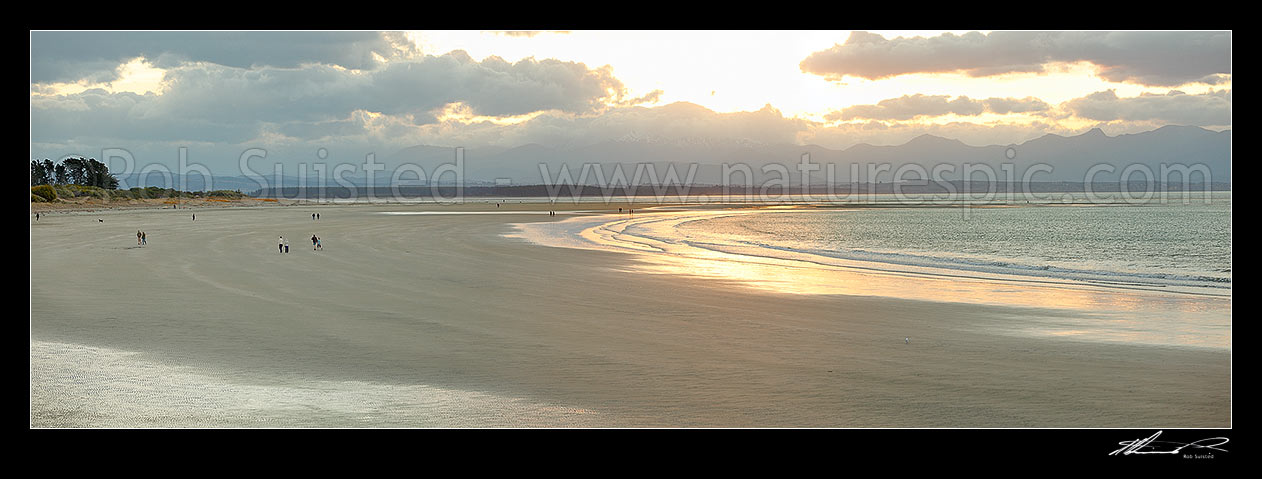 Image of Tahunanui Beach with people enjoying walking in the evening, with Arthur Range and Kahurangi National Park beyond. Panorama, Nelson, Nelson City District, Nelson Region, New Zealand (NZ) stock photo image