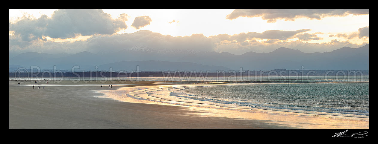 Image of Tahunanui Beach with people enjoying walking in the evening, with Arthur Range and Kahurangi National Park beyond. Panorama, Nelson, Nelson City District, Nelson Region, New Zealand (NZ) stock photo image