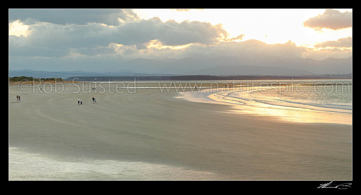 Image of Tahunanui Beach with people enjoying walking in the evening, with Arthur Range and Kahurangi National Park beyond. Panorama, Nelson, Nelson City District, Nelson Region, New Zealand (NZ) stock photo image