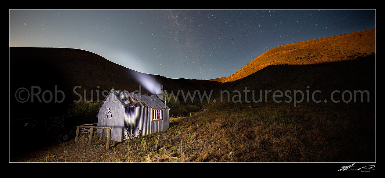 Image of Half Moon Hut at night with star trails above. Historic old musterers hut near the Dillion River, in Half Moon Stream. Panorama during moonrise, Molesworth Station, Marlborough District, Marlborough Region, New Zealand (NZ) stock photo image