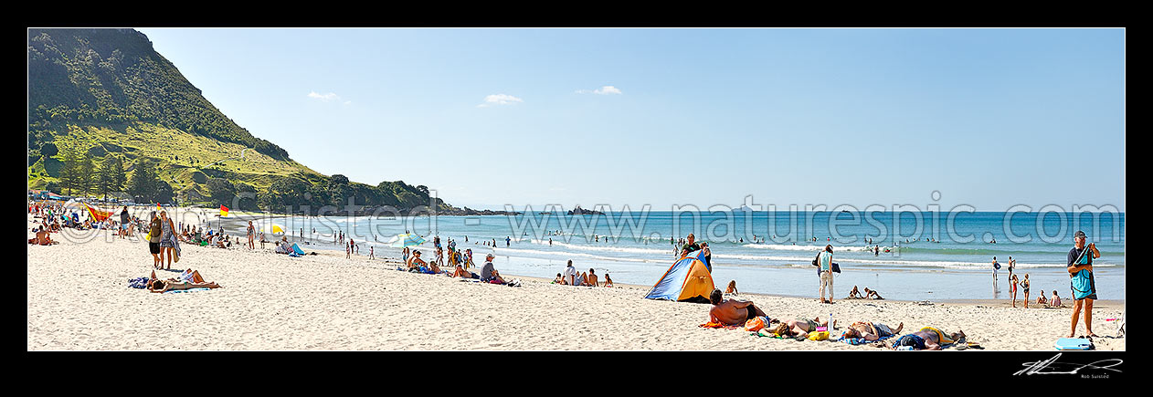 Image of Mount Maunganui beach panorama, with people sunbathing and swimming, and distant Karewa Island (centre) beyond. The Mount peak at left, Mount Maunganui, Tauranga District, Bay of Plenty Region, New Zealand (NZ) stock photo image