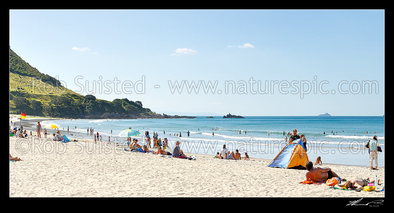 Image of Mount Maunganui beach panorama, with people sunbathing and swimming, and distant Karewa Island (right) beyond. The Mount peak at left, Mount Maunganui, Tauranga District, Bay of Plenty Region, New Zealand (NZ) stock photo image