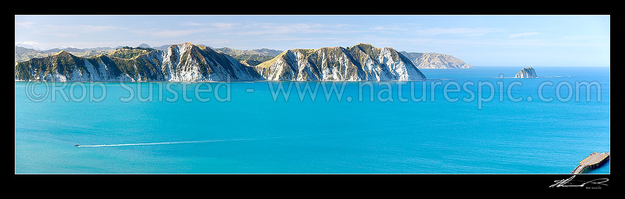 Image of Tolaga Bay. Marau Point visible beyond Te Karaka Point and island. Recreational fishing boat returning and old wharf visible far right. Panorama, Tolaga Bay, Gisborne District, Gisborne Region, New Zealand (NZ) stock photo image