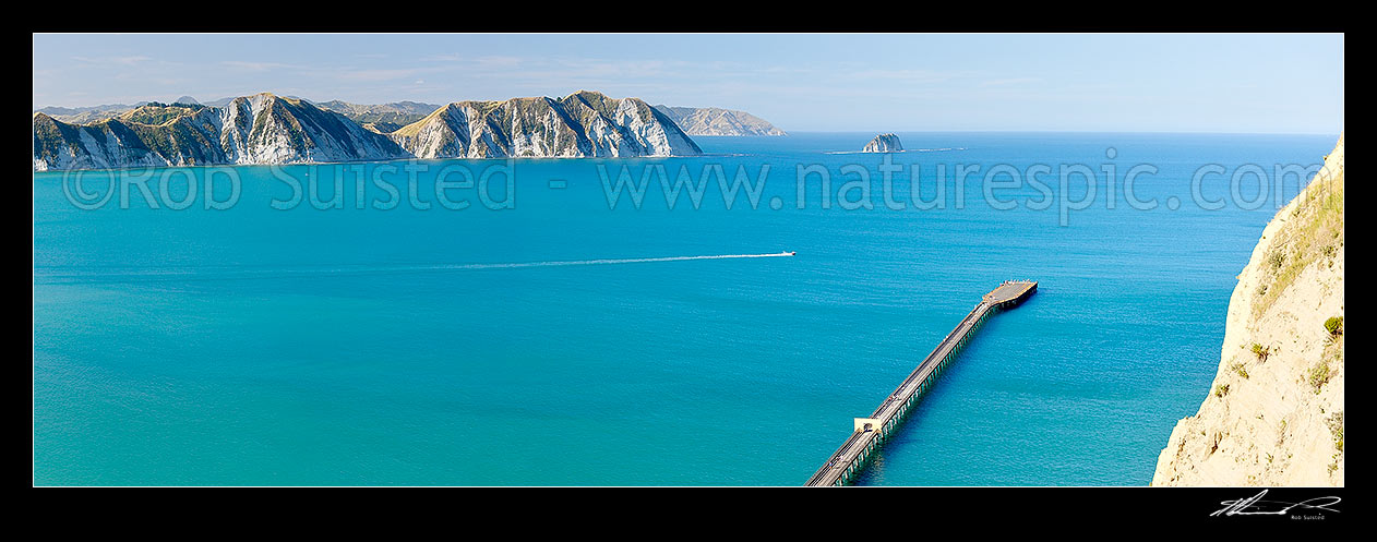 Image of Tolaga Bay. Marau Point visible beyond Te Karaka Point and island. Recreational fishing boat heading out past the old wharf. Panorama, Tolaga Bay, Gisborne District, Gisborne Region, New Zealand (NZ) stock photo image