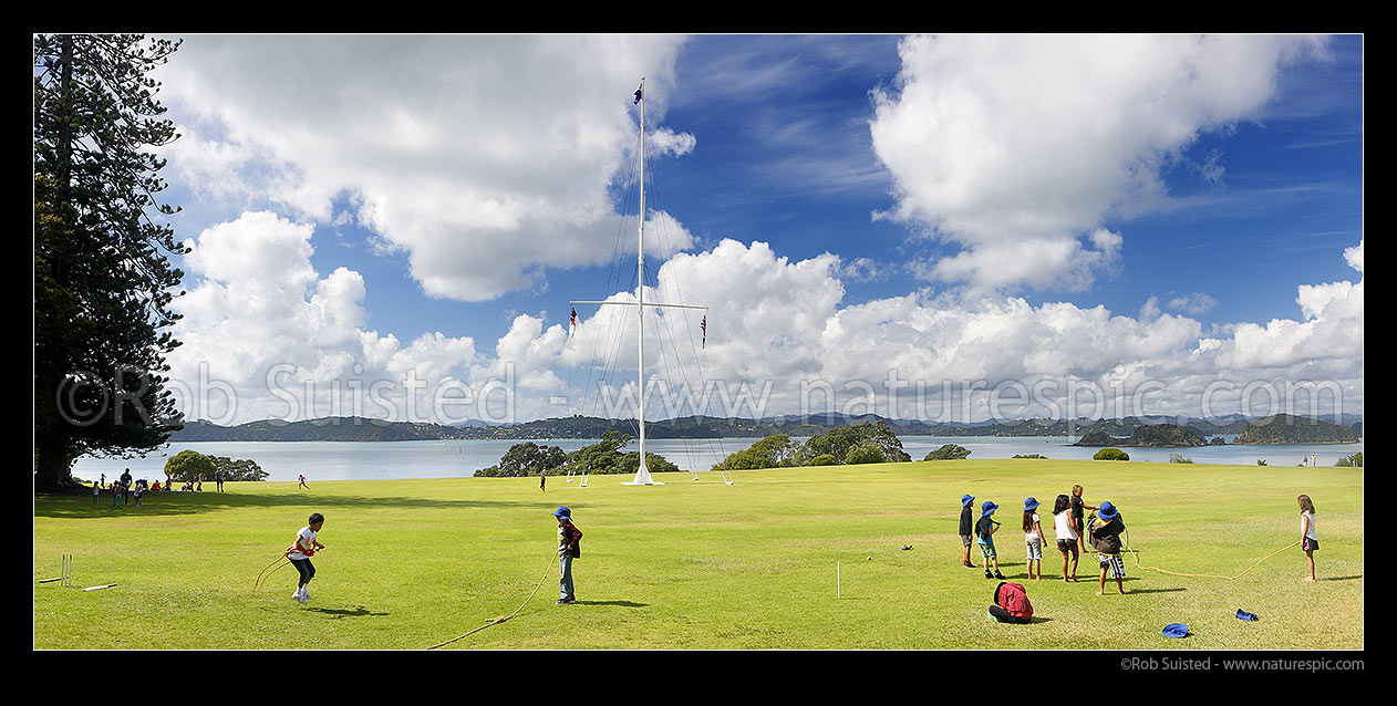 Image of Waitangi Treaty Grounds with visiting school children playing on grass. Naval flagstaff standing where Te Tiriti o Waitangi (Treaty of Waitangi) was signed. Panorama, Waitangi, Bay of Islands, Far North District, Northland Region, New Zealand (NZ) stock photo image