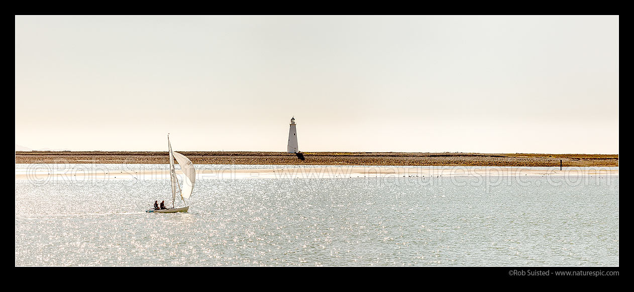 Image of Small sailboat sailing on Nelson Haven, with the Boulder Bank and historic 1862 lighthouse behind. Flying Dutchmen class NZL 106. Panorama, Nelson, Nelson City District, Nelson Region, New Zealand (NZ) stock photo image