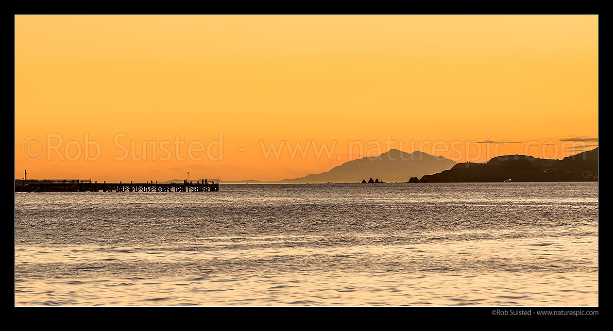 Image of Wellington Harbour entrance sunset. Eastbourne wharf with fishers and South Island Seaward Kaikoura Ranges in distance. Seatoun and Point Dorset at right. Panorama, Eastbourne, Hutt City District, Wellington Region, New Zealand (NZ) stock photo image