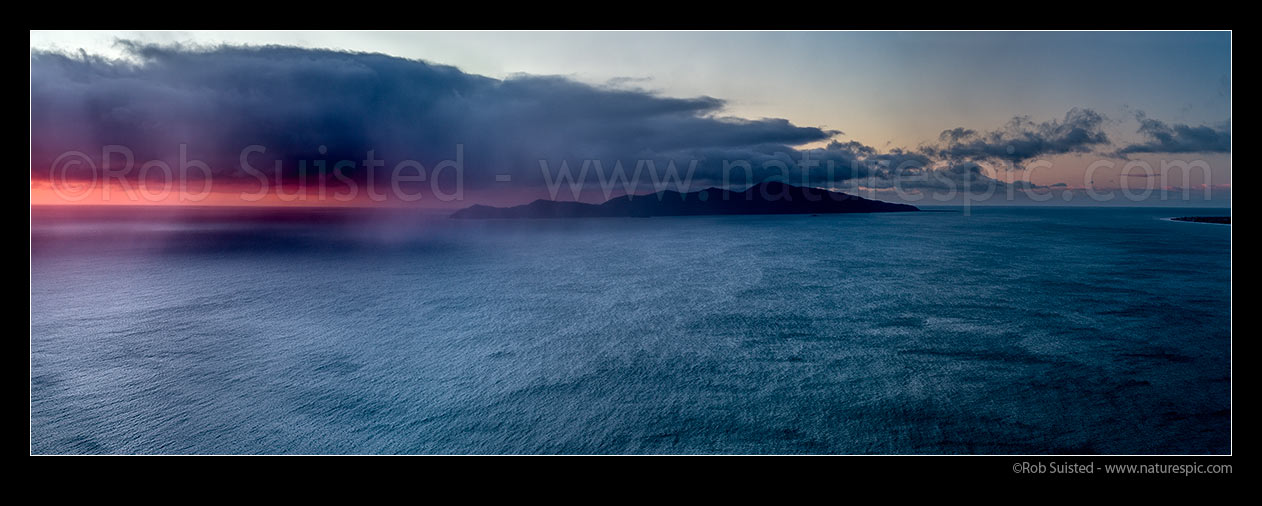 Image of Kapiti Island with sleety rain showers moving in from Cook Strait on a moody sunset. Rauoterangi Chanel (Otaheke Strait) at right. Panorama, Paekakariki, Kapiti Coast District, Wellington Region, New Zealand (NZ) stock photo image