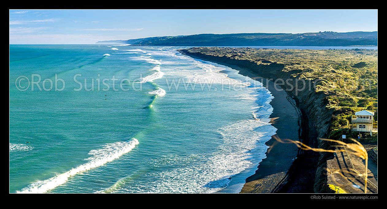 Image of Port Waikato beach in front of surf club, with surfers enjoying waves. Black ironsands beach and dunes with Waikato River mouth beyond, and Whatipu Heads in distance left. Panorama, Port Waikato, Franklin District, Waikato Region, New Zealand (NZ) stock photo image