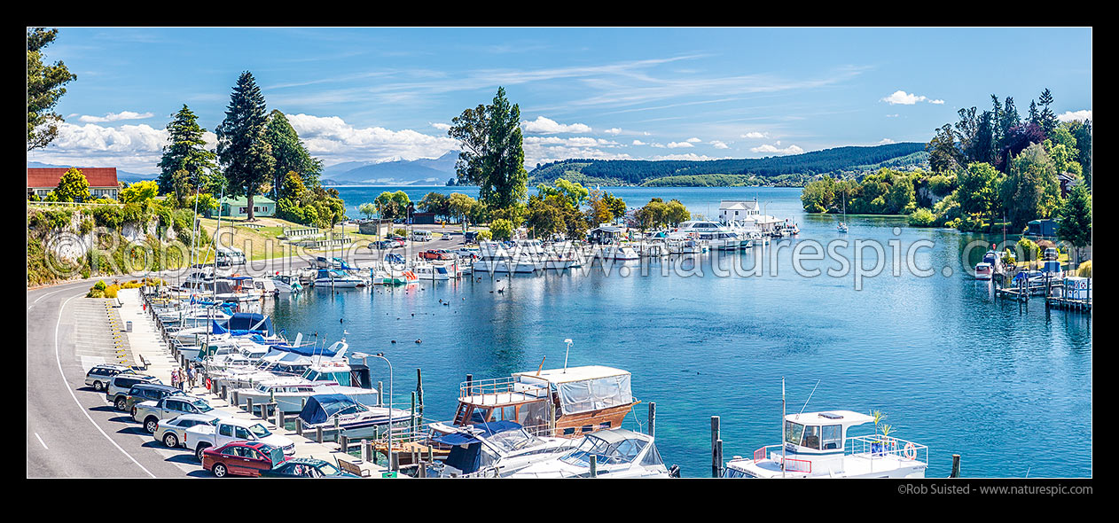 Image of Lake Taupo marina with boats moored at the start of the Waikato River. Tongariro National Park and volcanic peaks beyond. Panorama, Taupo, Taupo District, Waikato Region, New Zealand (NZ) stock photo image