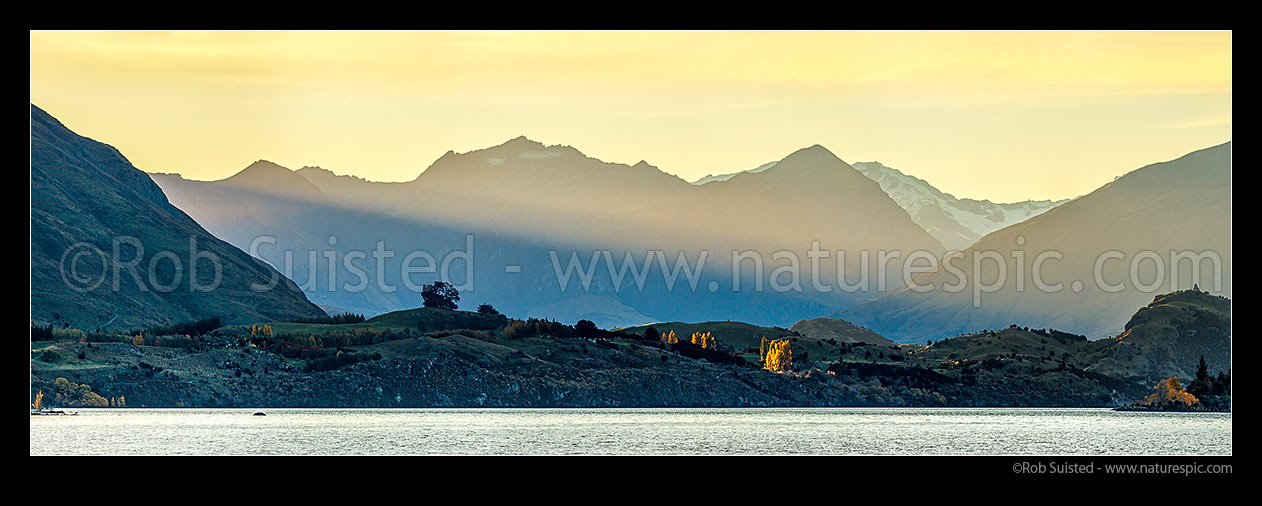 Image of Lake Wanaka, with last rays of sunlight raking across Sharks Tooth Peak, Fog Peak (2240m - centre) and Niger Peak (2018m). Matukituki Valley beyond. Autumn colours. Panorama, Wanaka, Queenstown Lakes District, Otago Region, New Zealand (NZ) stock photo image