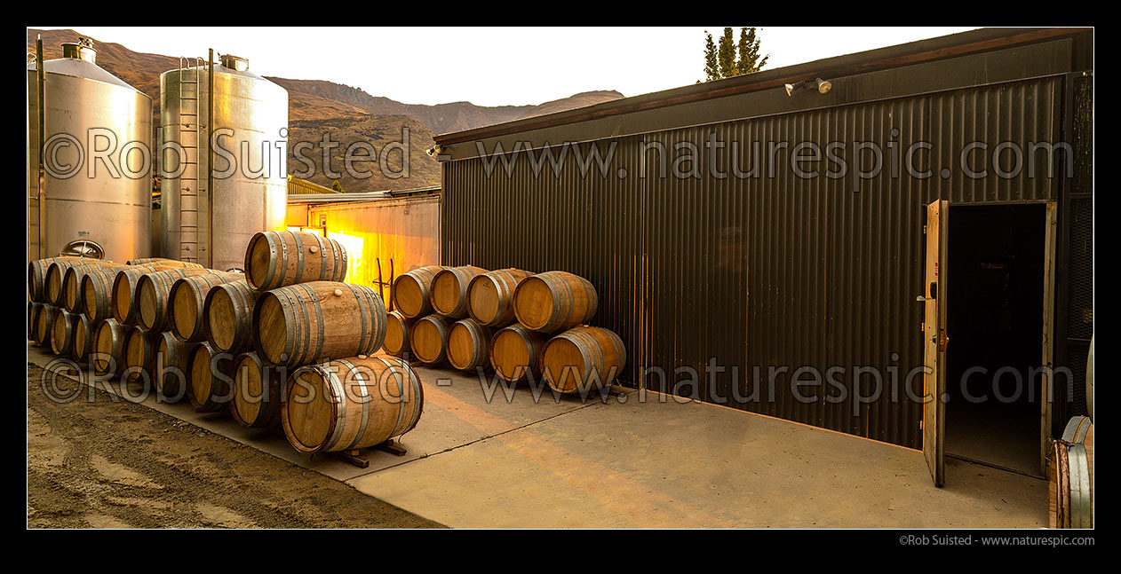 Image of Industrial commercial wine background with stainless steel tanks, vats and oak barrels stacked by warehouse at dusk. Panorama file, New Zealand (NZ) stock photo image