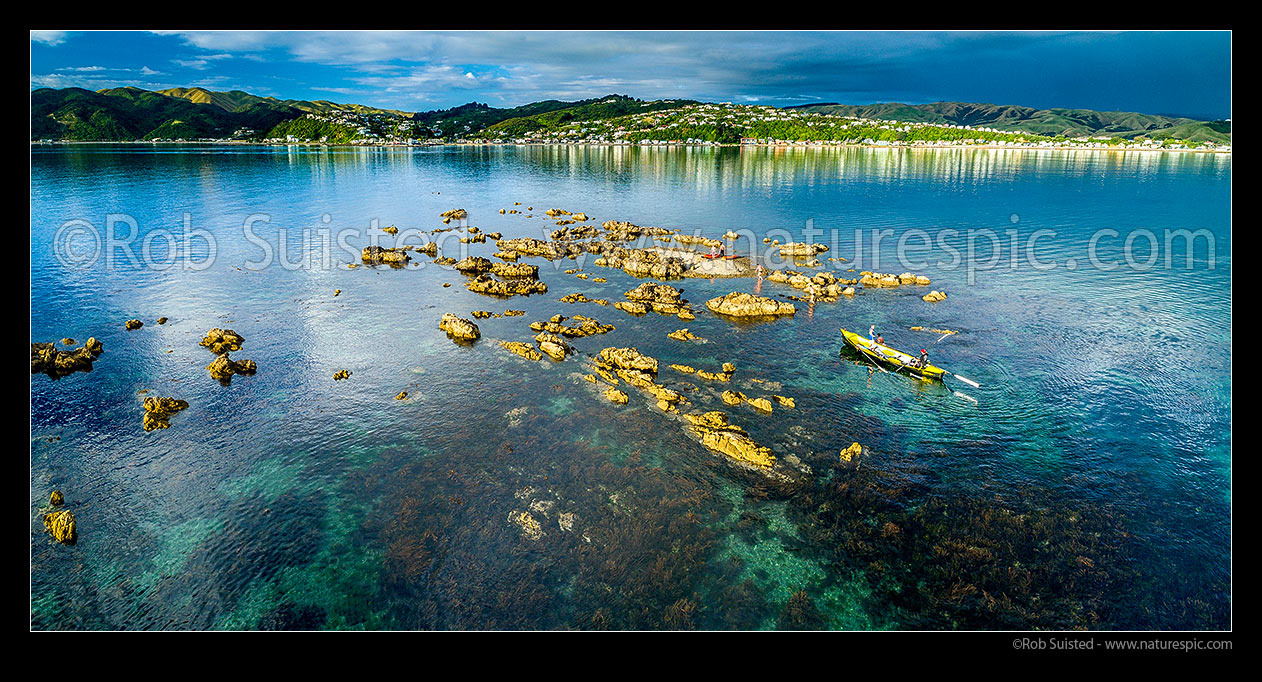 Image of Grandfather Rocks (Tokaapapa Reef) off Plimmerton Beach, with visitors in kayaks and surfboat enjoying the calm summer evening. Aerial panorama, Plimmerton, Porirua City District, Wellington Region, New Zealand (NZ) stock photo image