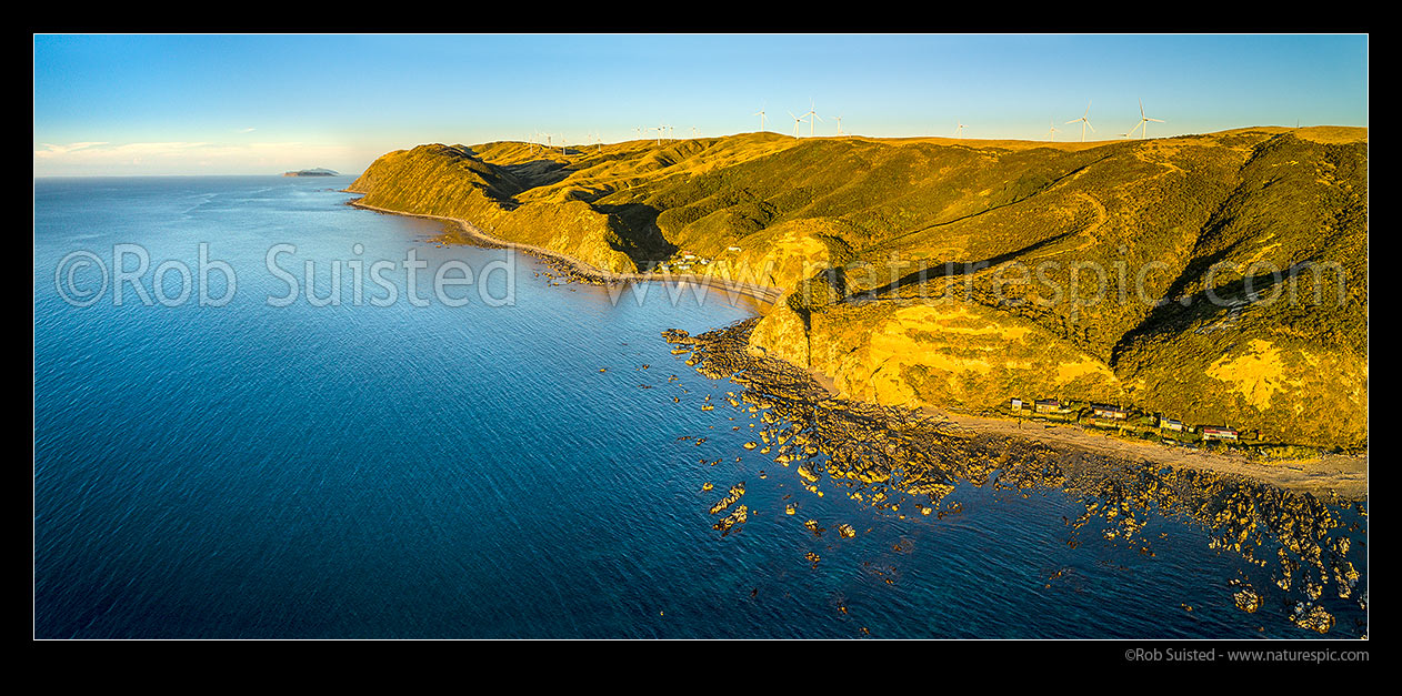 Image of Makara Beach coastline looking north from Ohariu Bay towards Mana and Kapiti islands. Smiths Bay and other baches under the Mill Creek Wind turbine farm. Aerial panorama, Makara Beach, Wellington City District, Wellington Region, New Zealand (NZ) stock photo image