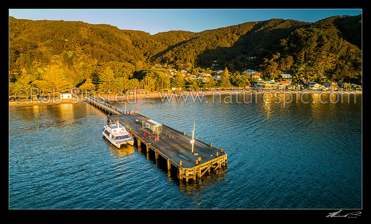 Image of Days Bay beach, bay and wharf with East by West Ferry alongside on a golden evening. Aerial panorama, Days Bay, Hutt City District, Wellington Region, New Zealand (NZ) stock photo image