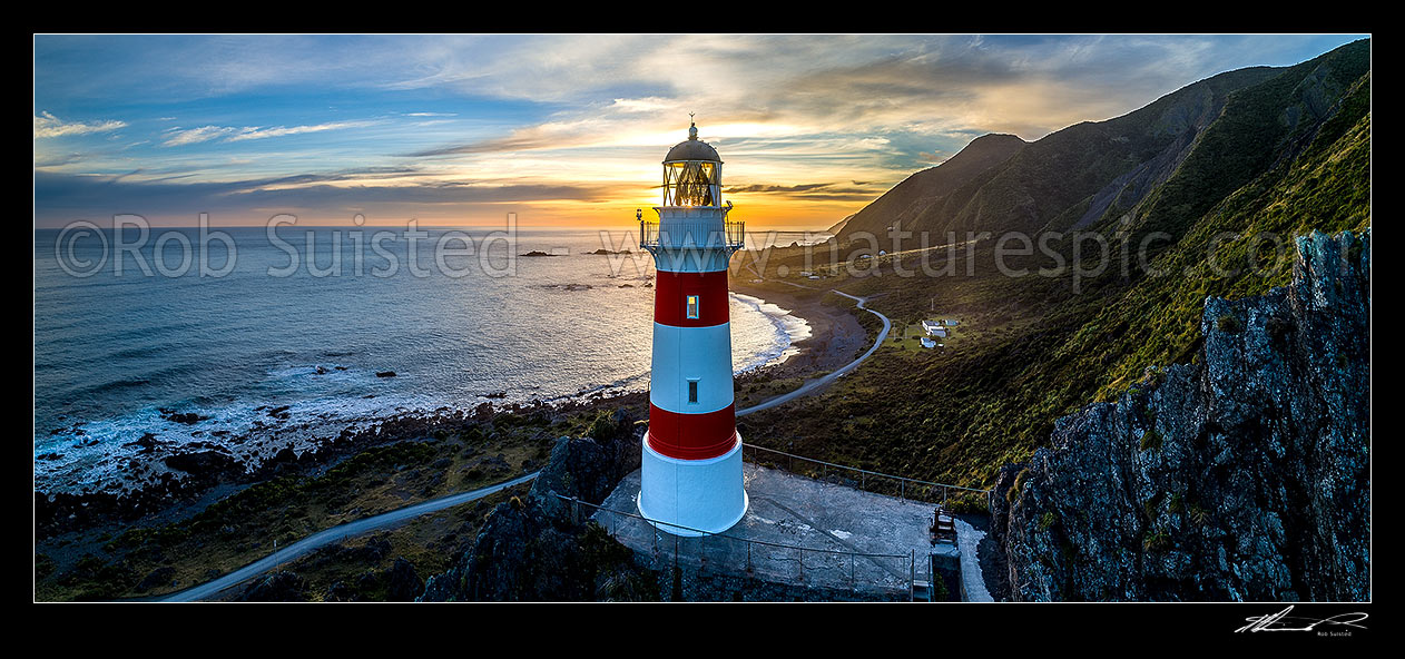 Image of Cape Palliser lighthouse standing above Palliser Bay baches and Kirikiri Bay at sunset (Matakitakiakupe). Aerial panorama with golden evening sunset, Cape Palliser, South Wairarapa District, Wellington Region, New Zealand (NZ) stock photo image