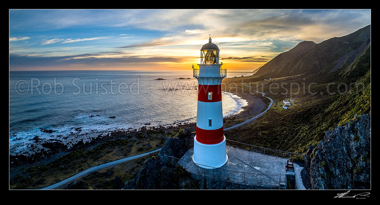 Image of Cape Palliser lighthouse standing above Palliser Bay baches and Kirikiri Bay at sunset (Matakitakiakupe). Aerial panorama with golden evening sunset, Cape Palliser, South Wairarapa District, Wellington Region, New Zealand (NZ) stock photo image